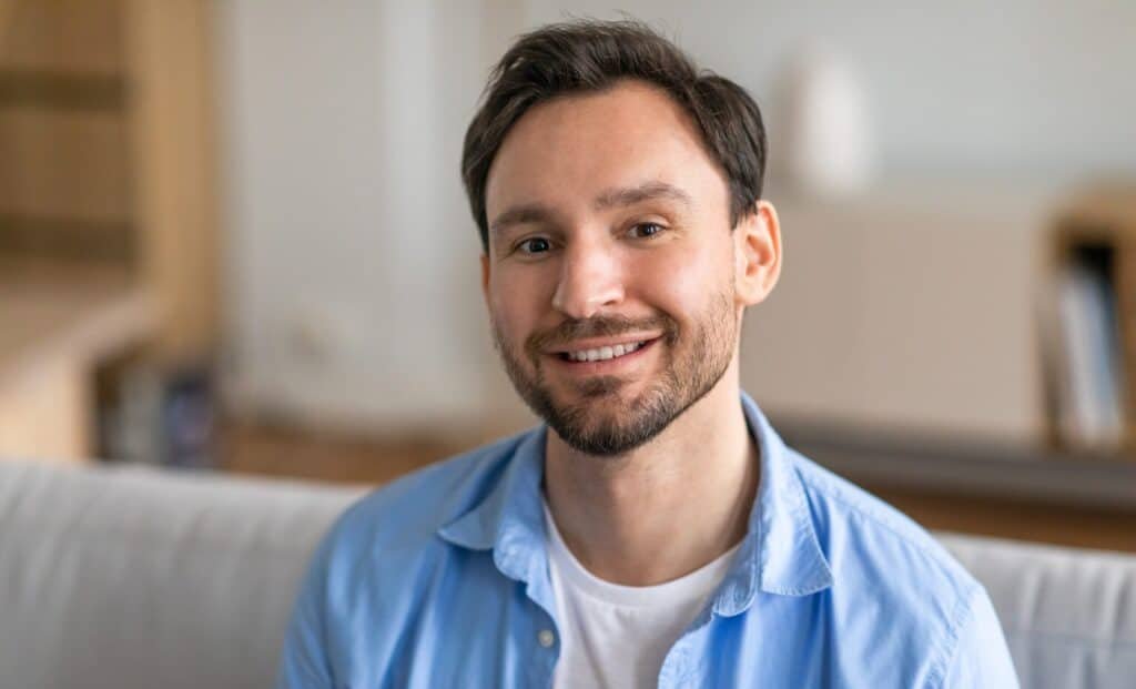 A,Man,Is,Seated,On,A,Couch,,Smiling,Joyfully.,He