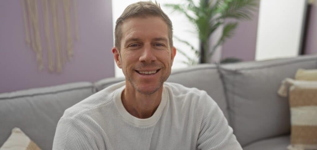 Handsome,Man,Smiling,On,Sofa,In,Modern,Living,Room,With
